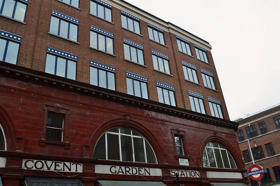 A multi-story brick building with numerous large, rectangular windows featuring blue-and-white striped awnings is seen from a low angle, emphasizing its height. The ground level displays a red-brick f